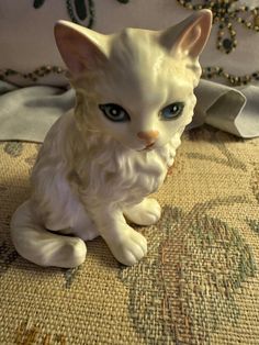 a white cat figurine sitting on top of a bed next to a pillow