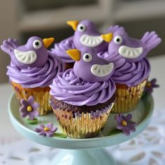 cupcakes with purple frosting decorated like birds on a green plate and white doily