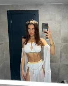 a woman taking a selfie in a bathroom mirror wearing a white outfit and gold jewelry