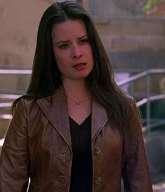 a woman wearing a brown leather jacket and black top standing in front of some stairs