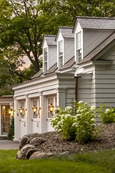 the front of a house with white siding and windows on each side, surrounded by lush green grass