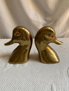 two brass ducks sitting on top of a white sheet