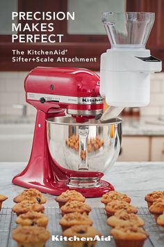 a red kitchen aid mixer sitting on top of a counter next to muffins