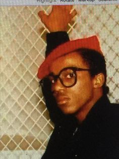 a man wearing glasses and a red hat with his hand up in front of him