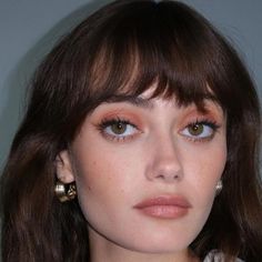 a close up of a person with brown hair and blue eyes wearing gold ear rings