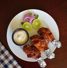 fried chicken on skewers with dipping sauce and onion rings are sitting on a white plate