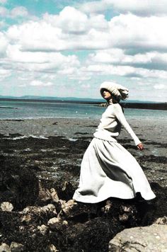 a woman in a long dress walking on rocks near the ocean