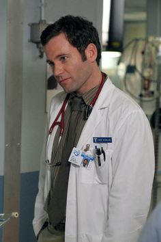 a man in a white lab coat standing next to a wall with medical equipment on it