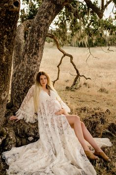 a woman is sitting under a tree wearing a white dress and posing for the camera