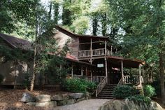 a large wooden house surrounded by trees in the middle of a wooded area with stairs leading up to it