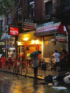 a person with an umbrella standing in front of a pizza shop on a rainy day