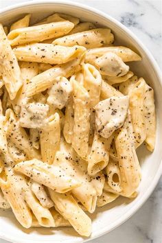 a white bowl filled with pasta covered in chicken and seasoning on top of a marble counter