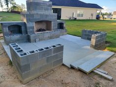 DIY Outdoor Fireplace in Backyard with cinderblock. Landscape rock and dirt construction zone. Grass, house, and trees in background with concrete patio and sitting wall in foreground. Maricopa design shown. Cinder Block Outdoor Fireplace, Diy Backyard Fireplace, Cinderblock House, Fireplace On A Budget, Outdoor Fireplace Diy, Fireplace Plans, Veneer Fireplace