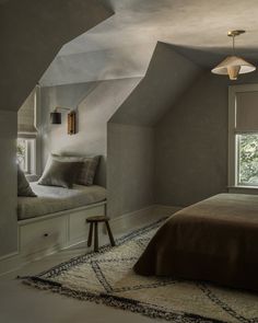 a bed sitting under a window in a bedroom next to a rug and lamp shade