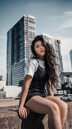 a woman sitting on top of a cement wall next to tall buildings in the background