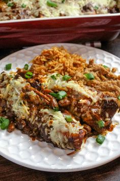 a white plate topped with rice and meat covered in sauce next to a casserole dish