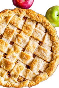 an apple pie with latticed crust and two green apples in the background on a white surface