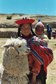 a woman with a child on her back and a llama in the foreground