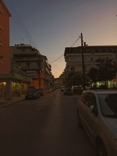 cars are parked on the side of an empty street at dusk with buildings in the background