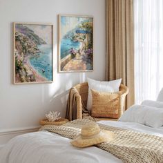 two paintings hang on the wall above a bed with white linens, pillows and blankets