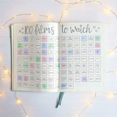 an open planner with the words 100 films to watch written on it next to a string of lights