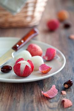 a white plate topped with red and white desserts next to a knife on top of a wooden table