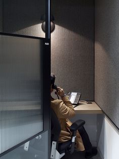 a person sitting at a desk with a laptop and cell phone to their ear, in an office cubicle