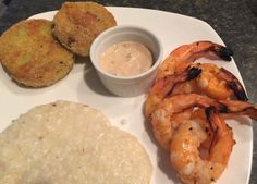 a white plate topped with shrimp, rice and two fried patties next to a bowl of dipping sauce