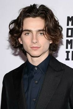 a young man with curly hair wearing a black suit