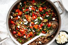 a pot filled with meat, vegetables and feta cheese on top of a table