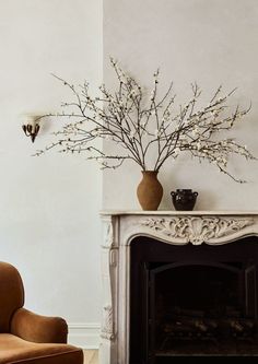 a living room with a fire place, chair and vase on the mantel in front of it