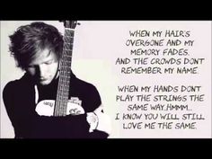 a man holding an acoustic guitar in front of a wall with words written on it