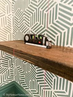 a clock sitting on top of a wooden shelf in front of a wallpapered wall