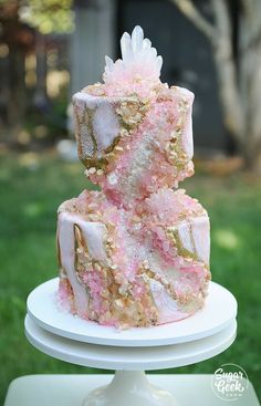 a three tiered cake with pink and gold frosting on top sitting on a white plate