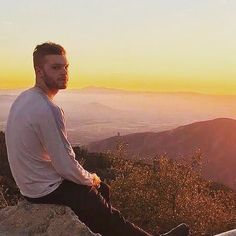 a man sitting on the edge of a cliff at sunset