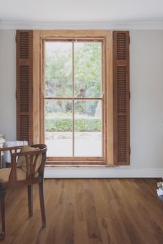 a chair sitting in front of a window with shutters on the windowsill and wood flooring