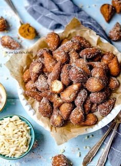 powdered sugar coated doughnuts in a bowl on a blue table with spoons