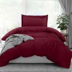 a bed with red comforter and pillows in front of a large window on a carpeted floor