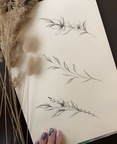 a woman's hand holding a piece of paper next to some dried flowers and grasses