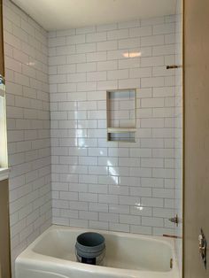 a bathroom with white tiles and a tub in it's corner, next to a window