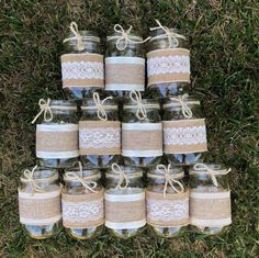 mason jars with lace and burlocks are arranged in a pyramid on the grass