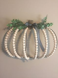 a wooden beaded pumpkin hanging on a wall with greenery and ribbon tied around it