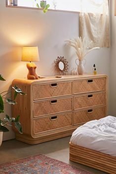 a bedroom scene with focus on the dresser and bed side table, which has a plant next to it