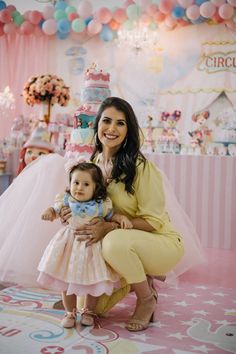 a woman holding a small child in front of a birthday cake display at a party