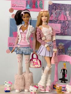 two barbie dolls standing next to each other in front of a wall with pictures on it