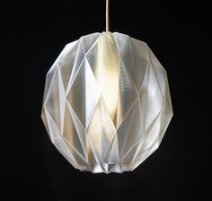 a white origami light hanging from a black ceiling with a gold colored cord