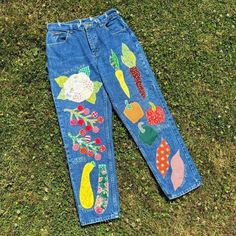 a pair of blue jeans with embroidered fruits and vegetables on them sitting in the grass