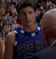 a young man in a basketball uniform talking to an older man