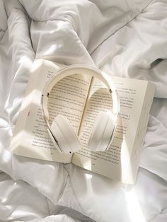 an open book with headphones on top of it sitting on a white comforter