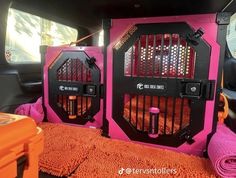 two pink and black cages in the back of a car with orange towels on the floor